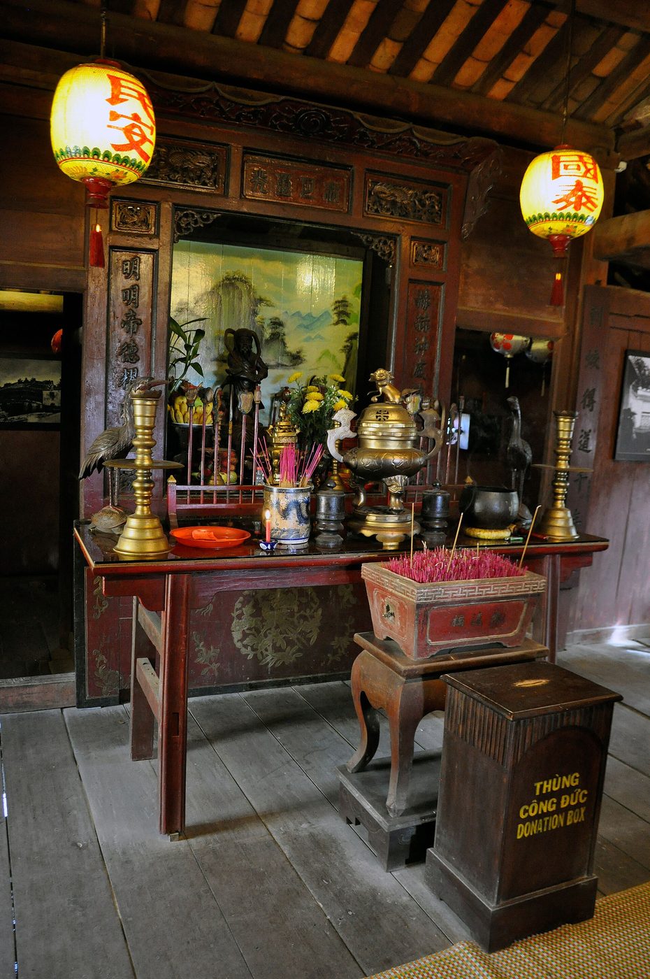 The altar inside the bridge: dark statue of the deity behind brass candlesticks, incense pots and two paper lanterns.