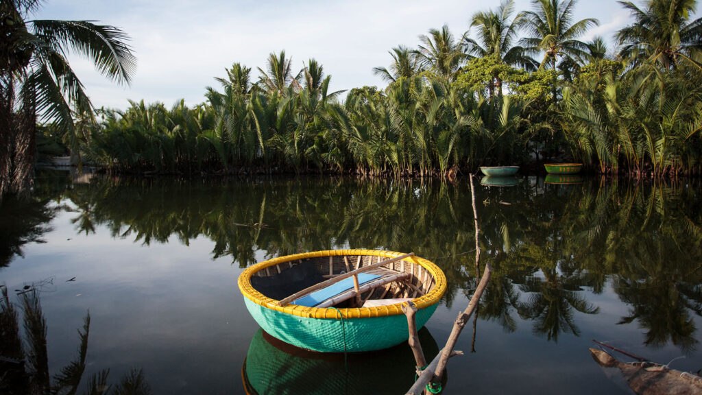 A still creek mirroring dense nipa palm along both banks, a basket boat moored near shore, two more anchored further out.