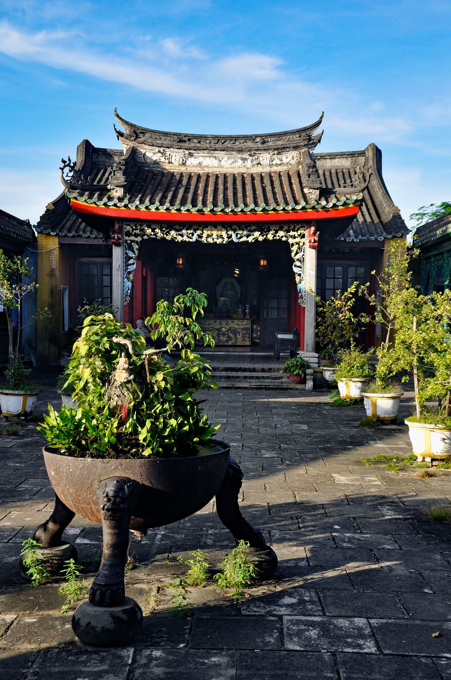 The front of the Trung Hoa hall in Hội An, pale washed walls, a tiled porch over the main door with a Chinese board above it, red lanterns along the eaves.