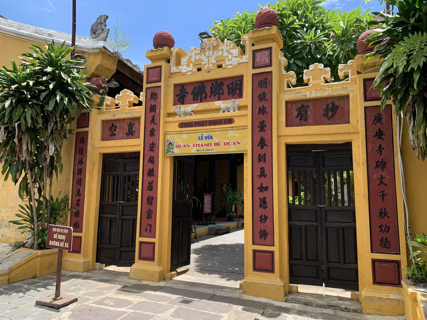 The front of the Quan Công temple in Hội An, yellow walls, a triple gate under tubular tiles with modelled figures along the ridge, Chinese couplets flanking the door.
