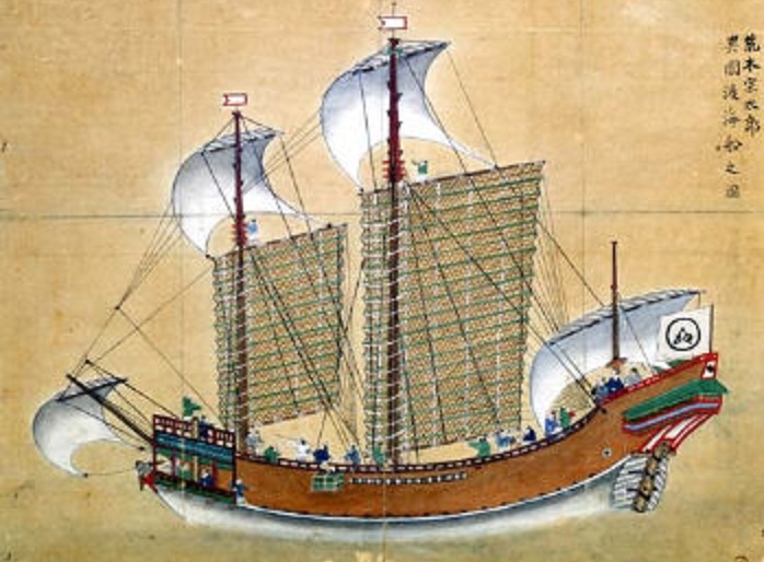 A colour painting of an ocean trading ship: brown hull, two large ribbed lattice sails, several white cloth sails, and crew in blue and green standing along the deck. A white flag at the stern carries a black monogram inside a circle. Four lines of Chinese characters stand in the upper right corner.