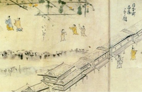 Handscroll detail labelled 日本町: a row of tiled roofs along the water, figures walking a raised street, and travellers on a plain above.