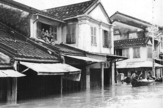 The junction under water in 1964: people sitting in an upstairs window above the awnings, a sampan being poled along what was the street.