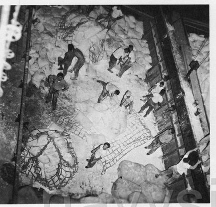 Looking straight down into the hold of the USS Princeton: a man stands on a hill of sacks, the cargo net spread out across the deck.