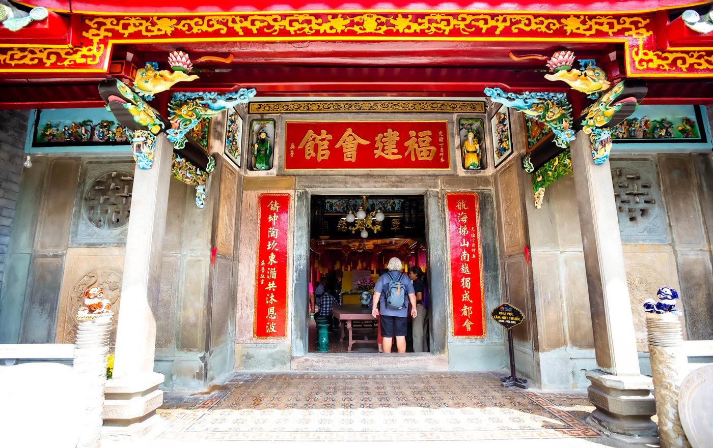 The main entrance of the assembly hall, a gold-on-red horizontal plaque above the door reading the hall's name in Chinese characters, red vertical couplets framing the doorway on both sides.