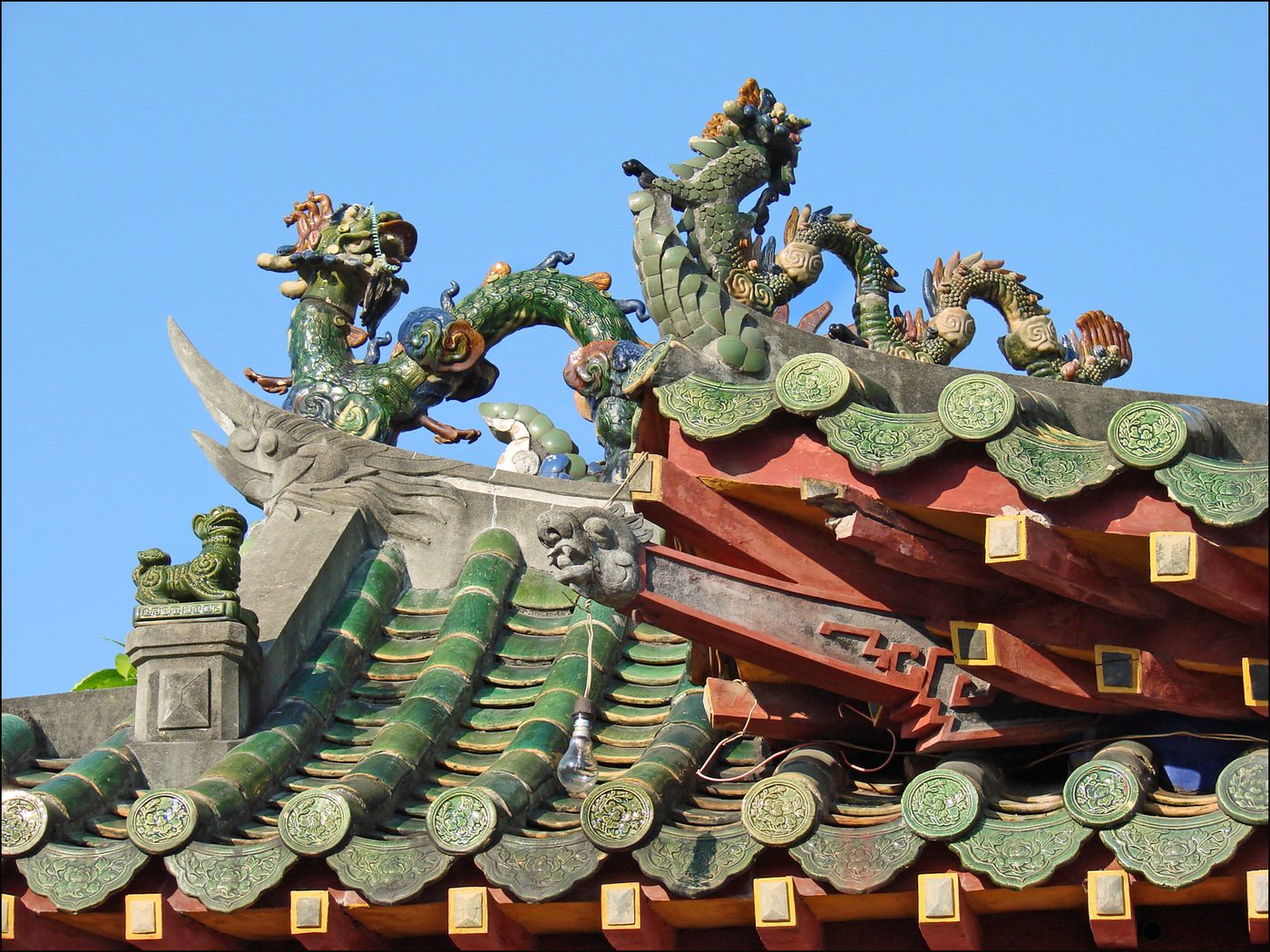 A close view of a ceramic-mosaic dragon and phoenix riding the curved roof ridge of the front hall, glazed green barrel tiles below, medallion end-tiles along the eave.