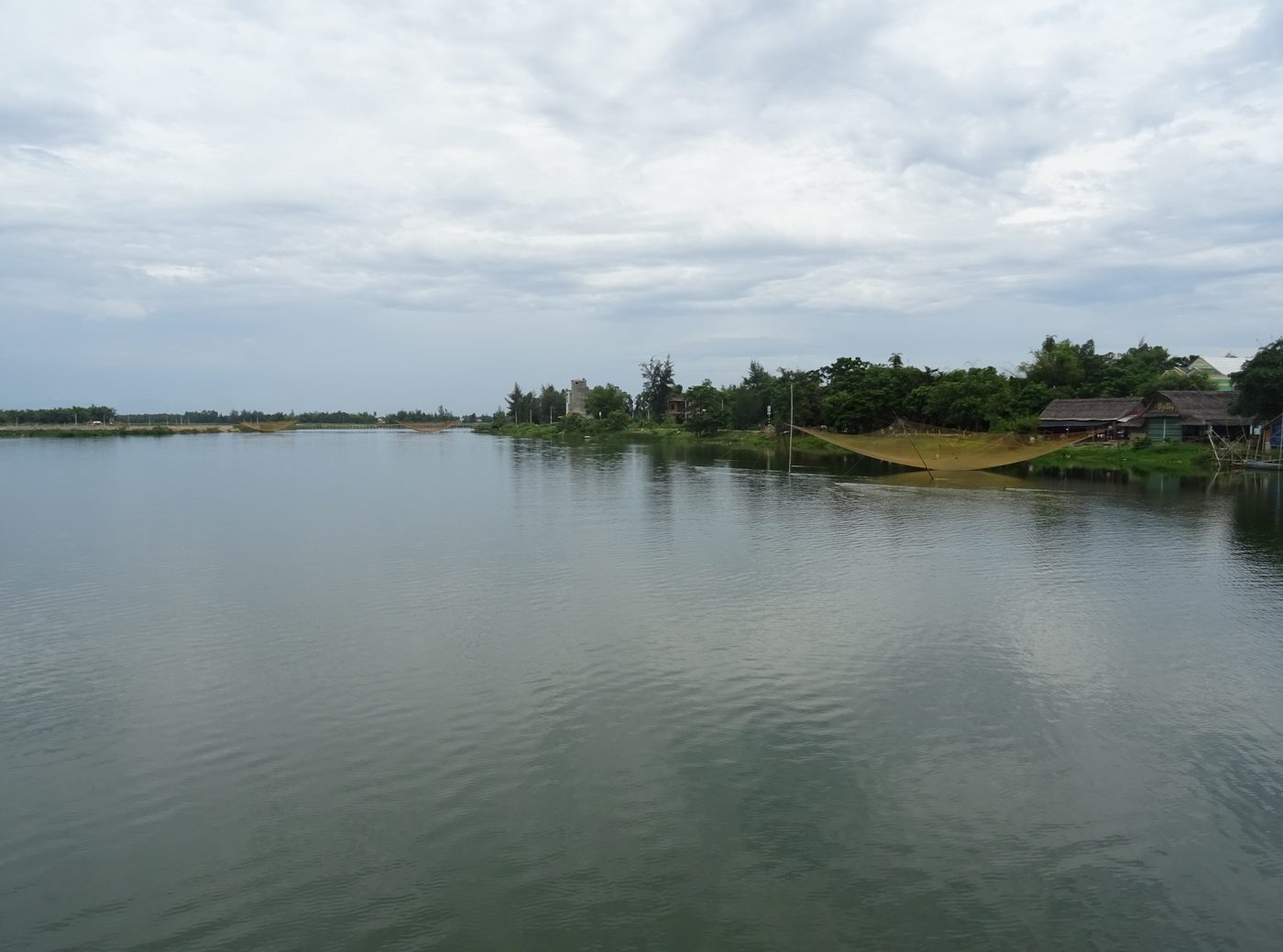 The Thu Bồn seen from a bridge in Duy Xuyên district, a broad flat reach of water with fishing-net frames standing in it and low hills beyond.